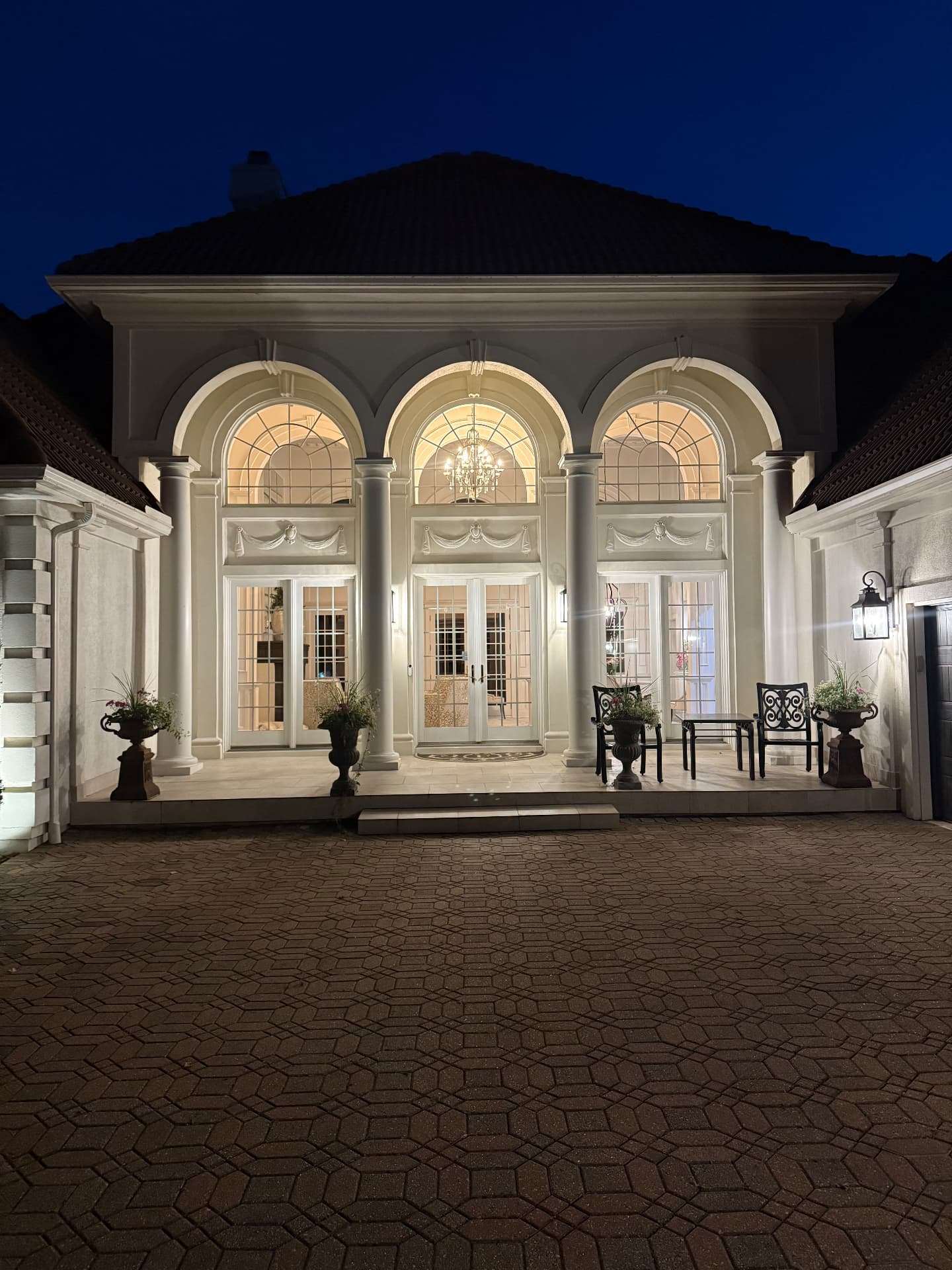 Illuminated arched portico at night with clean windows and paver driveway
